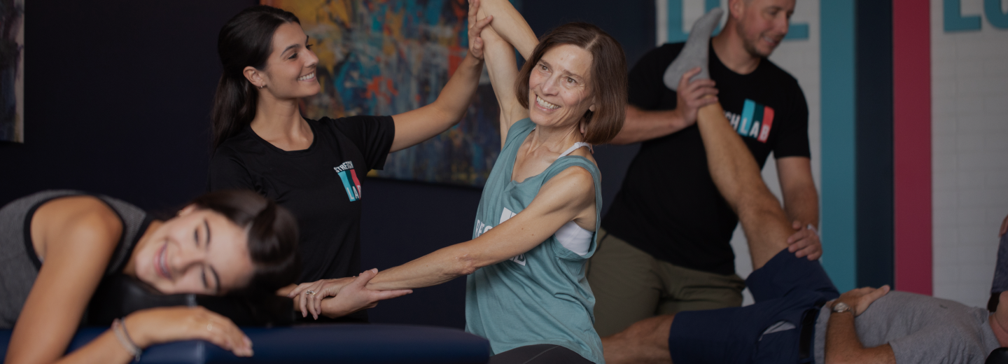 StretchLab stretch practitioners assisting two women and one man in stretch exercises