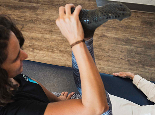 aerial of 50 year old female smiling with comfort & relief, receiving hamstring stretches from expert flexologist on padded bench at stretchlab studio