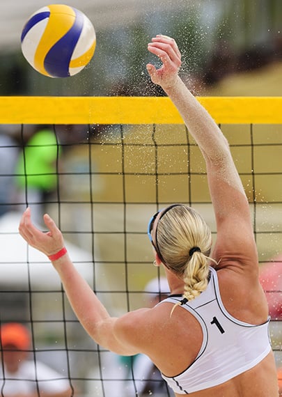 female volleyball player jumping up to hit a ball across the net