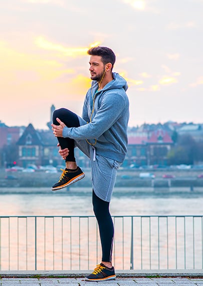 male runner stretching his legs in front of a waterway with a sunset